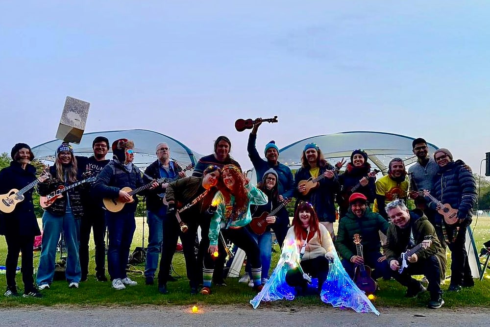 Ukulele Tuesday's community group, about twenty people with ukuleles, in front of a lit gazebo at dawn in Marlay Park
